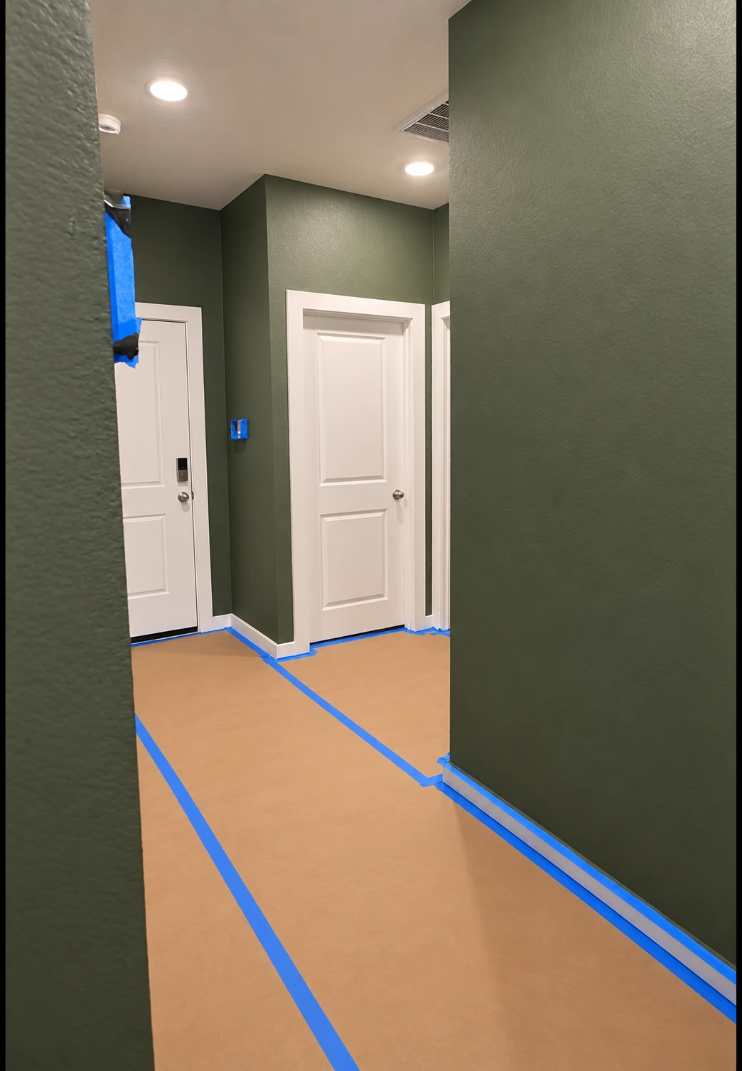 Interior hallway painting with olive green walls, white trim and floors protected with paper and blue tape · Cypress Tx